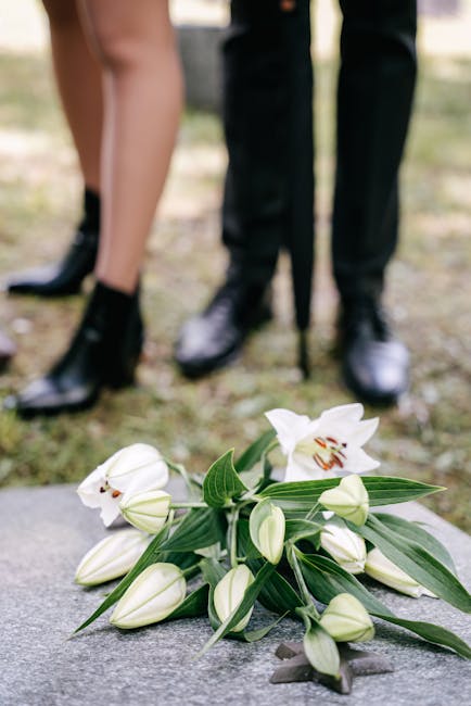 A delicate bouquet of white lilies with green leaves, arranged on a stone surface, featuring fully bloomed flowers with open petals and several closed buds. The bouquet appears fresh, with smooth, sli